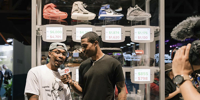 two men standing in front of shoes; one has a microphone